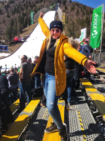 Predstavljaj si zgodnje jutro, ko se odpraviš proti Planici. Cesta proti dolini je že polna ljudi v slovenskih zastavah, kapah in šalih. V zraku je čutiti vznemirjenje – vsi vedo, da prihaja velik dan smučarskih skokov. Ko prideš v dolino pod velikanko -Letalnico bratov Gorišek, te najprej zadene razgled. Ogromna letalnica, obdana z zasneženimi vrhovi Julijskih Alp, tribune pa že polne navijačev. Povsod se sliši glasba in navijanje. Vonj po čaju, kuhanem vinu in klobasah se meša z mrzlim gorskim zrakom.Ko se začne tekma, nastane poseben trenutek tišine. Skakalec se spusti po zaletišču, množica pa zadrži dih. Ko skoči, vsi spremljajo skok — in ko pristane daleč, se tribune spremenijo v eksplozijo veselja. Slovenske zastave zaplapolajo, ljudje skačejo, se objemajo in kričijo. 